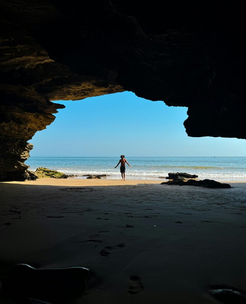 A person silhouetted in a cave opening at a beach in Taghazout, Morocco.