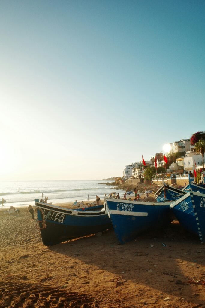 Blue fishing boats on sandy Taghazout beach during sunny day in Morocco.